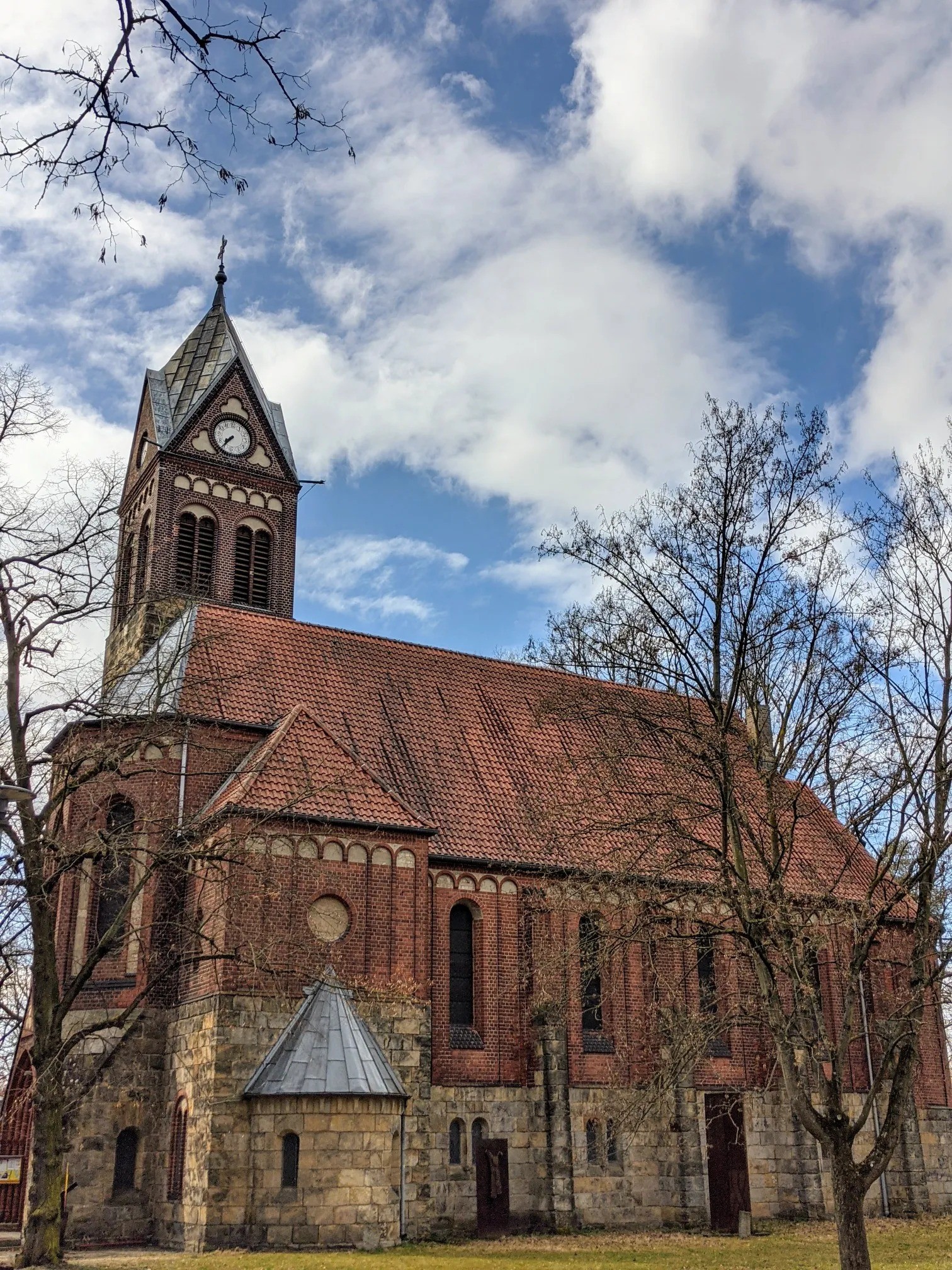 Backsteinkirche mit Feldsteinsockel und Uhrturm, davor kahle Bäume