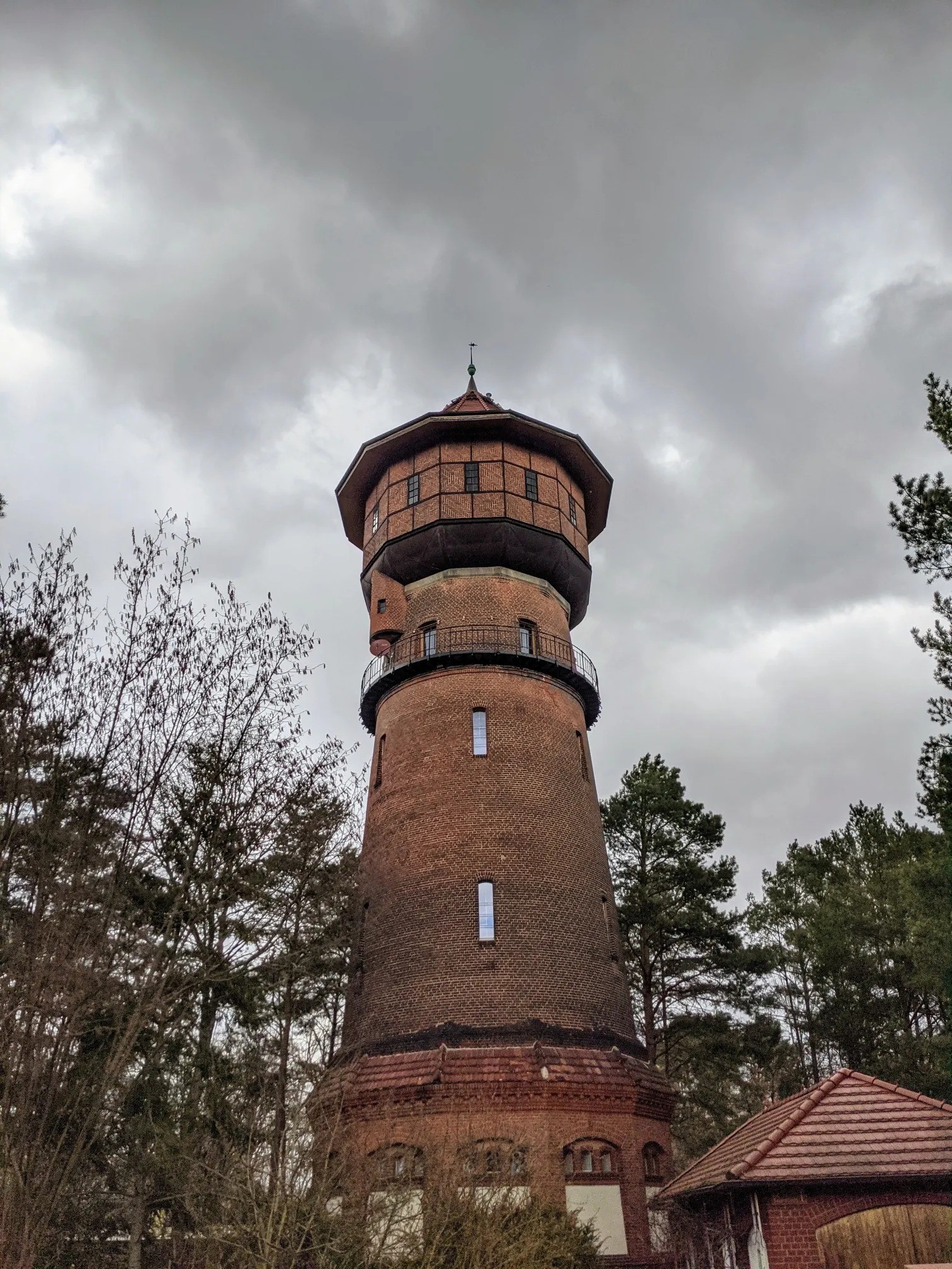 Runder Backsteinturm mit Fachwerkaufsatz und Umlaufbalkon zwischen Kiefern