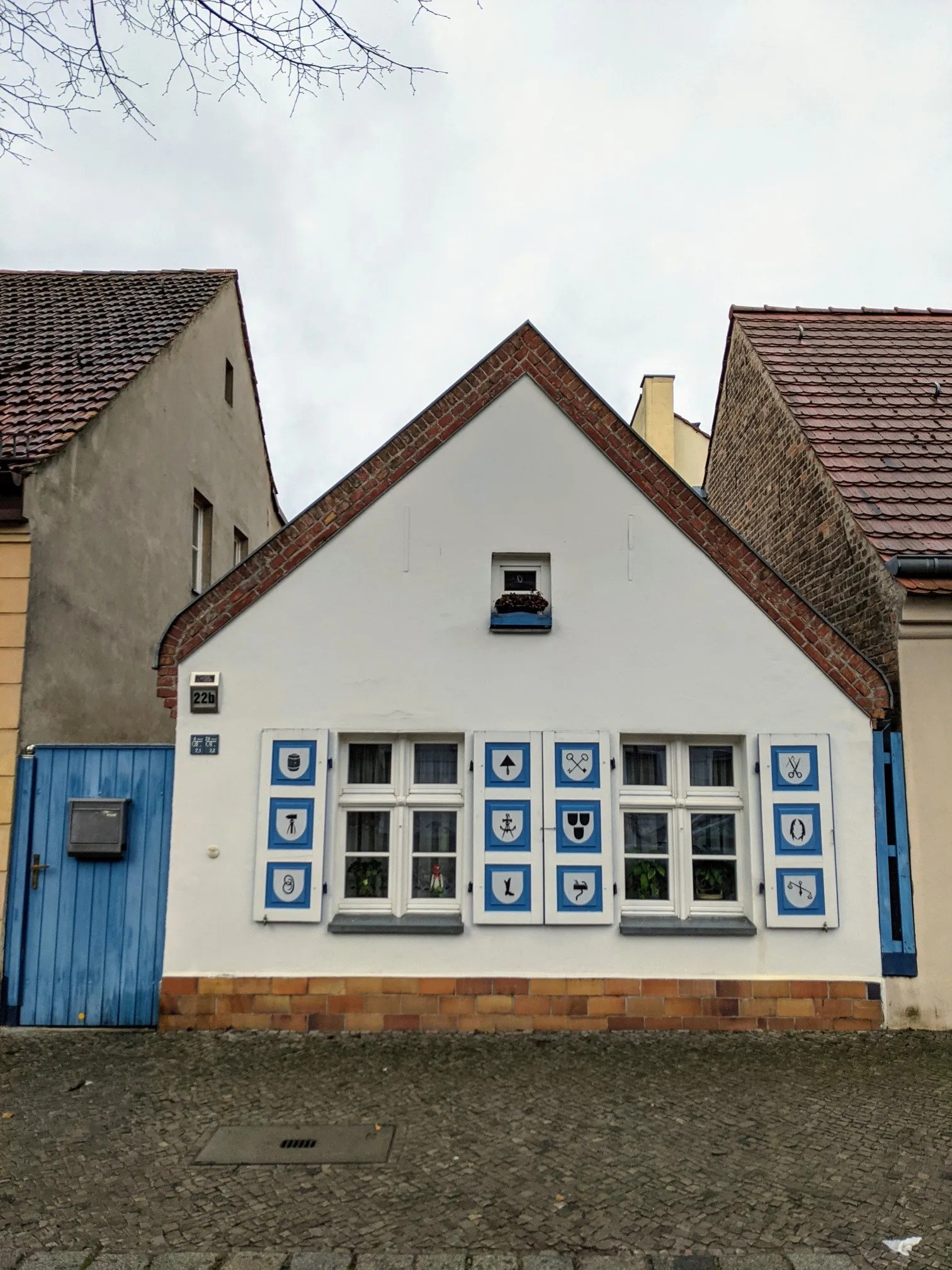 Weißes Giebelhaus mit Fensterläden, auf denen Handwerkszeichen aufgemalt sind