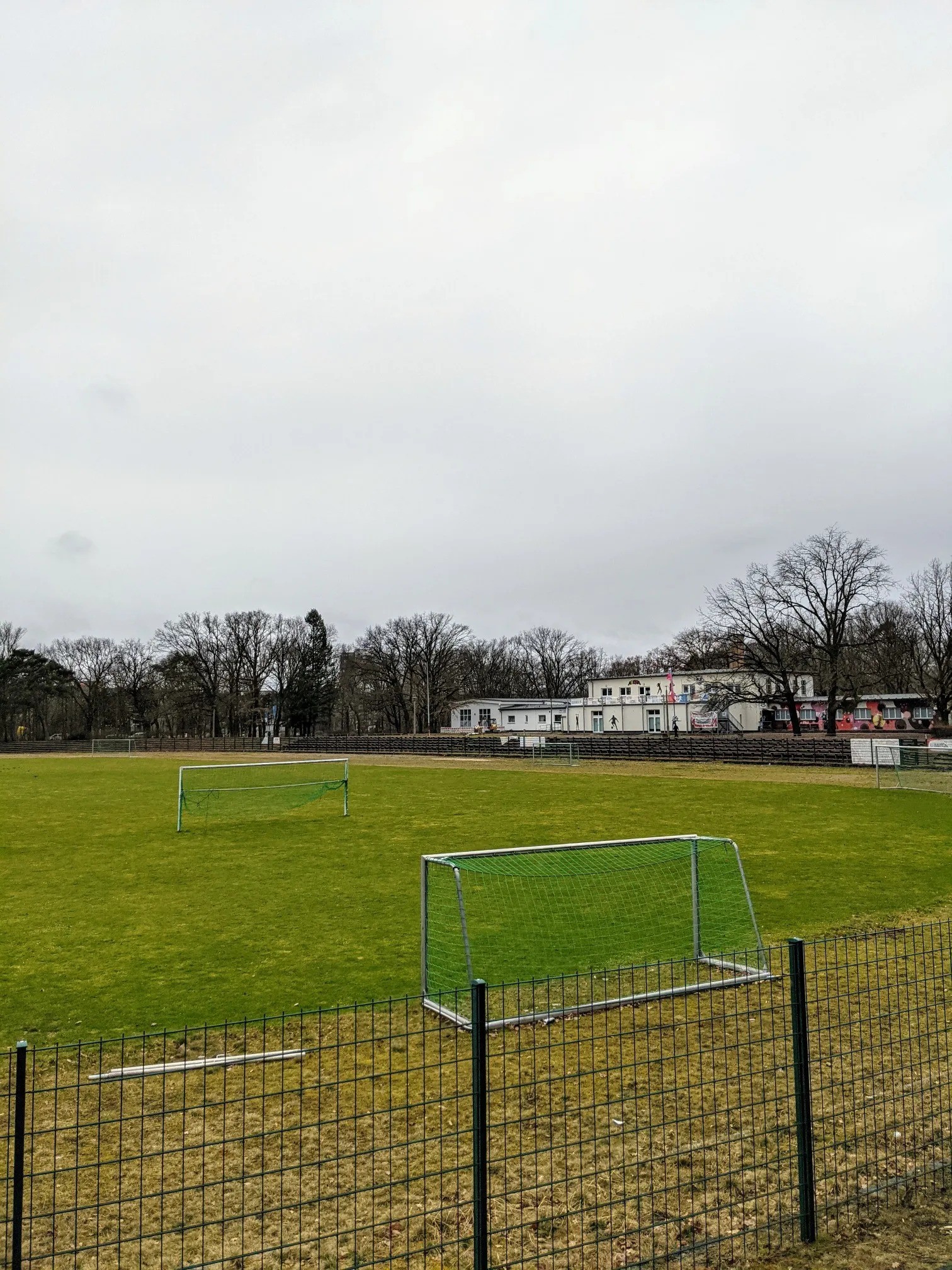 Sportplatz mit Fußballtoren und Vereinsheim unter grauem Himmel