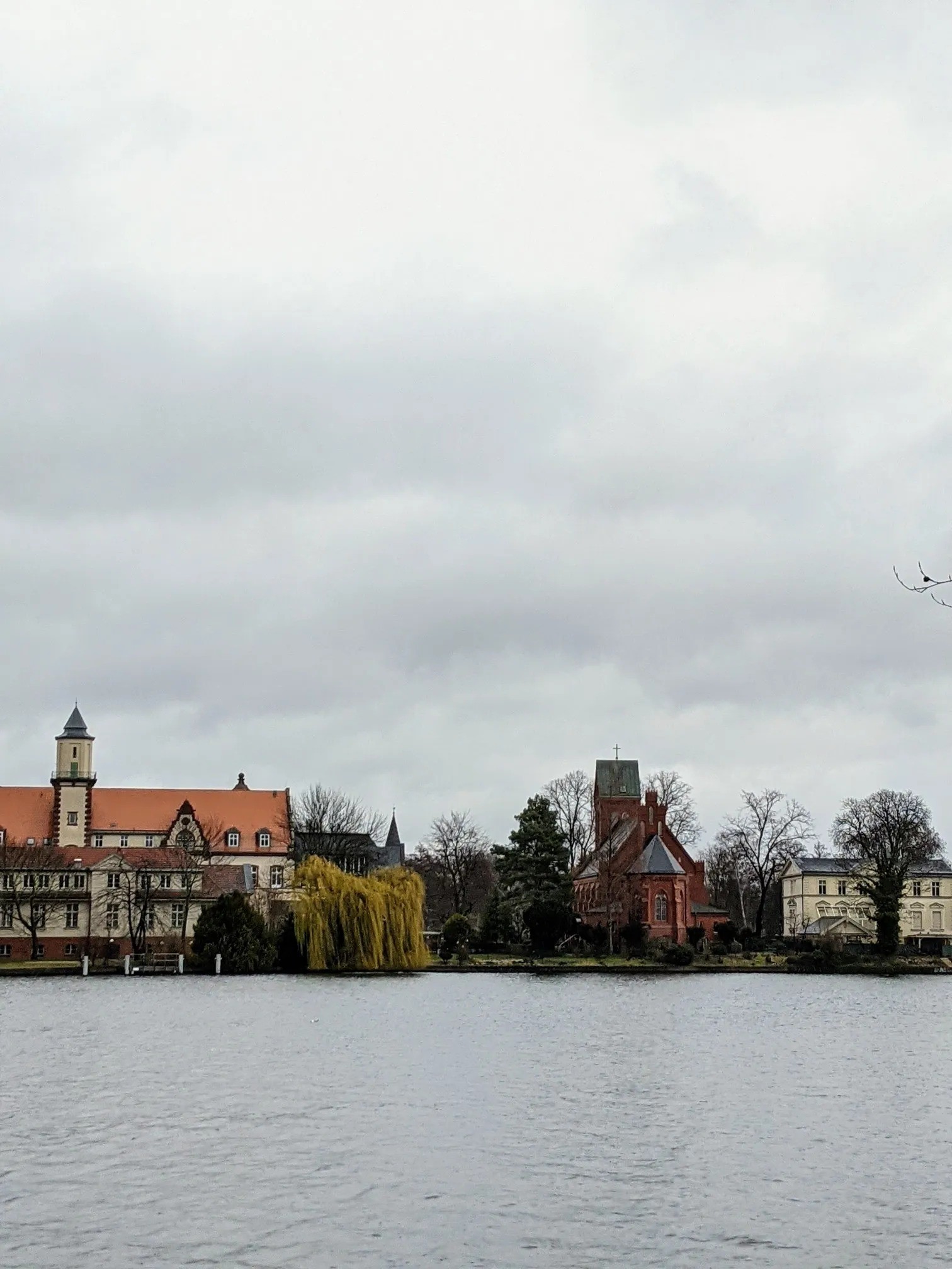 Ufer mit Gebäude, Trauerweide und roter Backsteinkirche