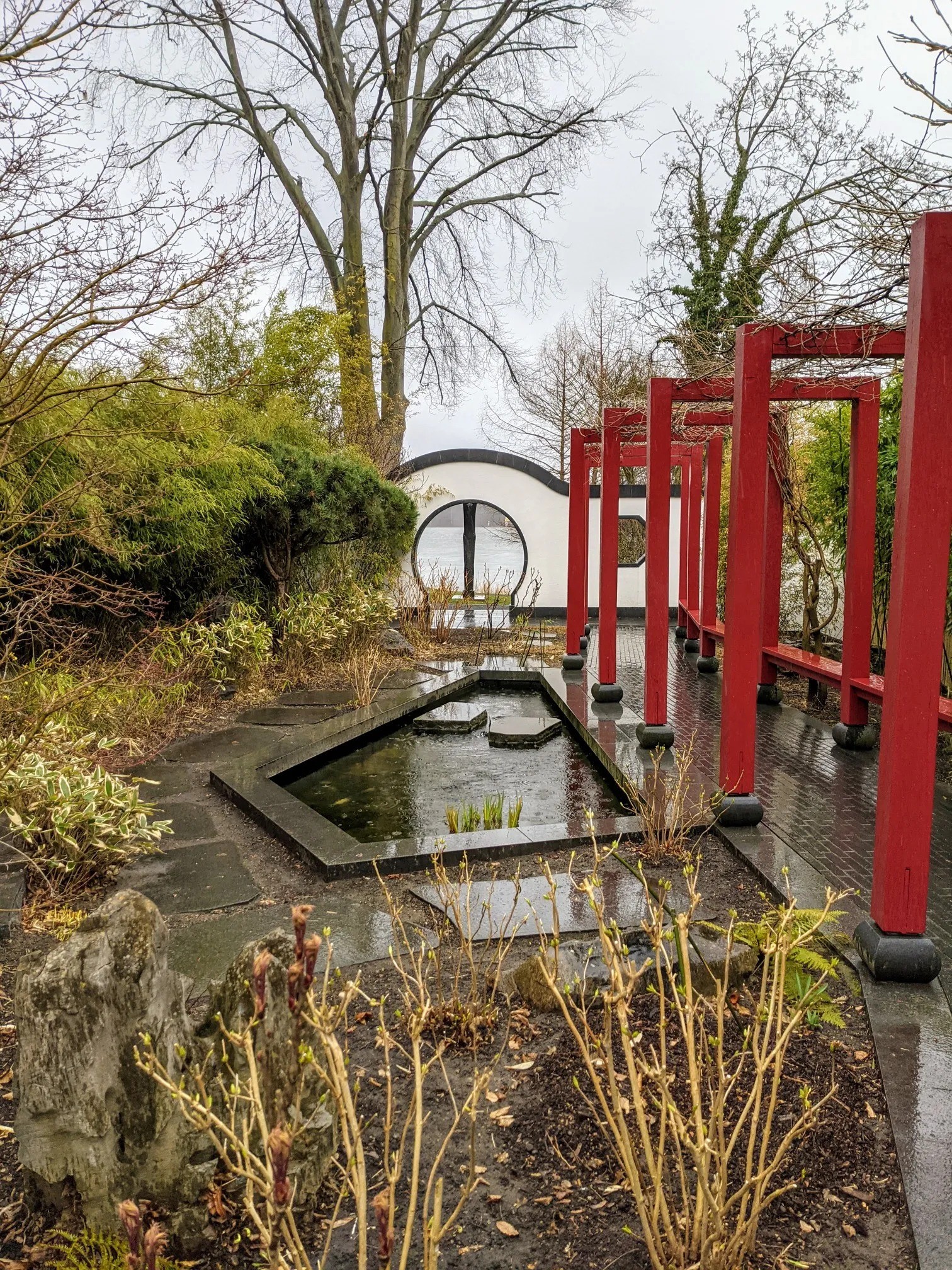 Chinesischer Garten mit roter Holzpergola, Wasserbecken und rundem Mondtor