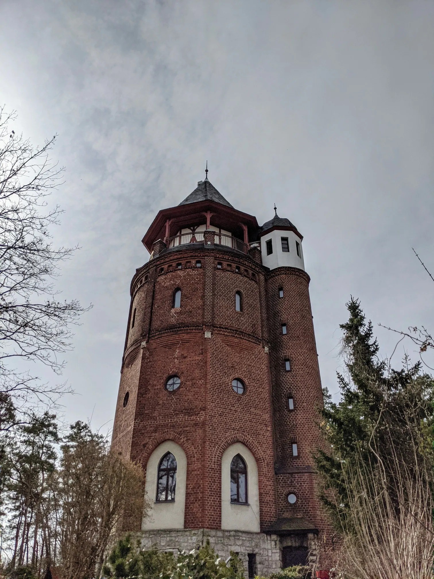Runder Backsteinturm mit hölzernem Umlaufgang und weißem Erkertürmchen vor bewölktem Himmel