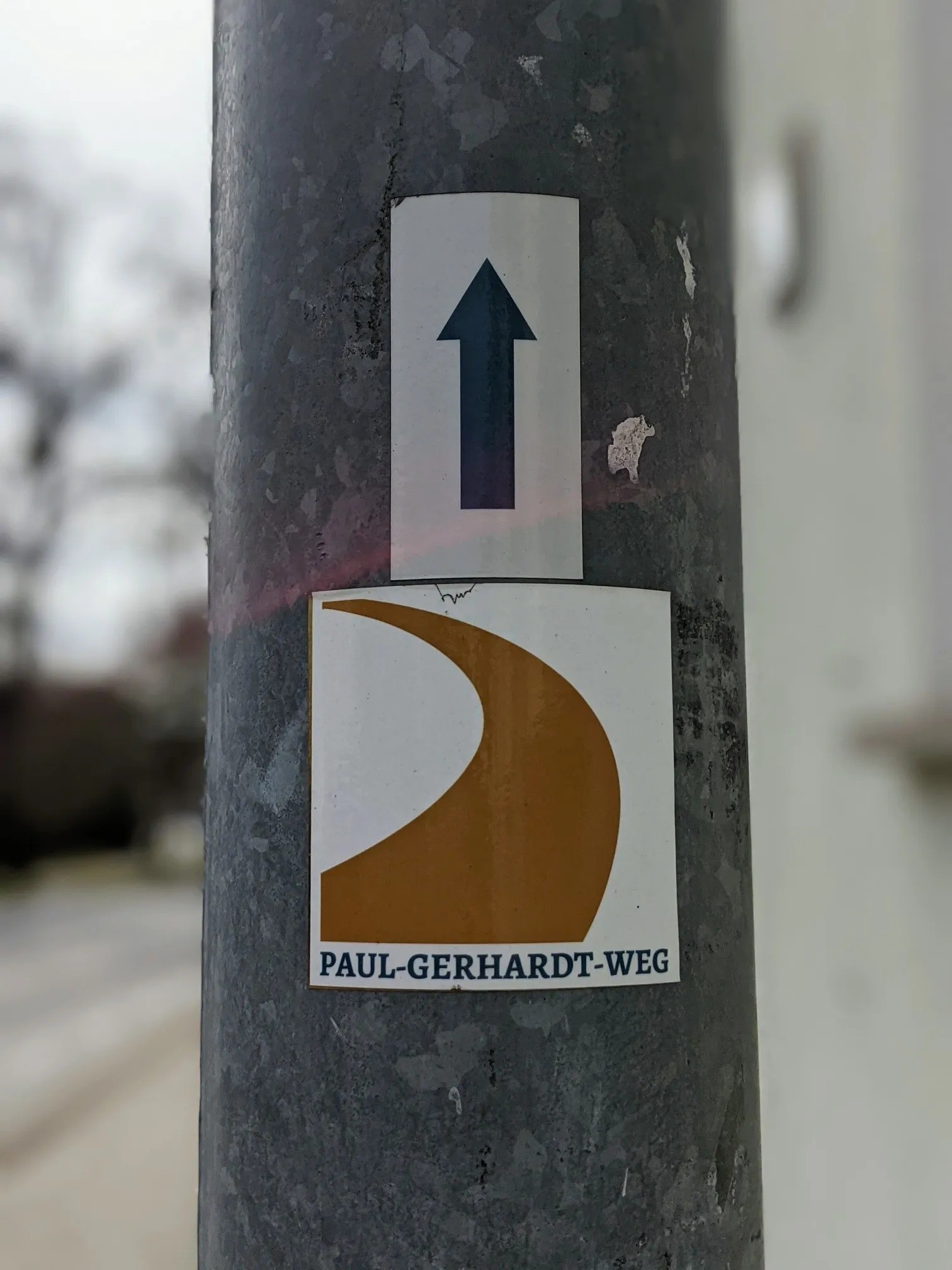 Laternenmast mit zwei Aufklebern: Richtungspfeil und Wegzeichen PAUL-GERHARDT-WEG
