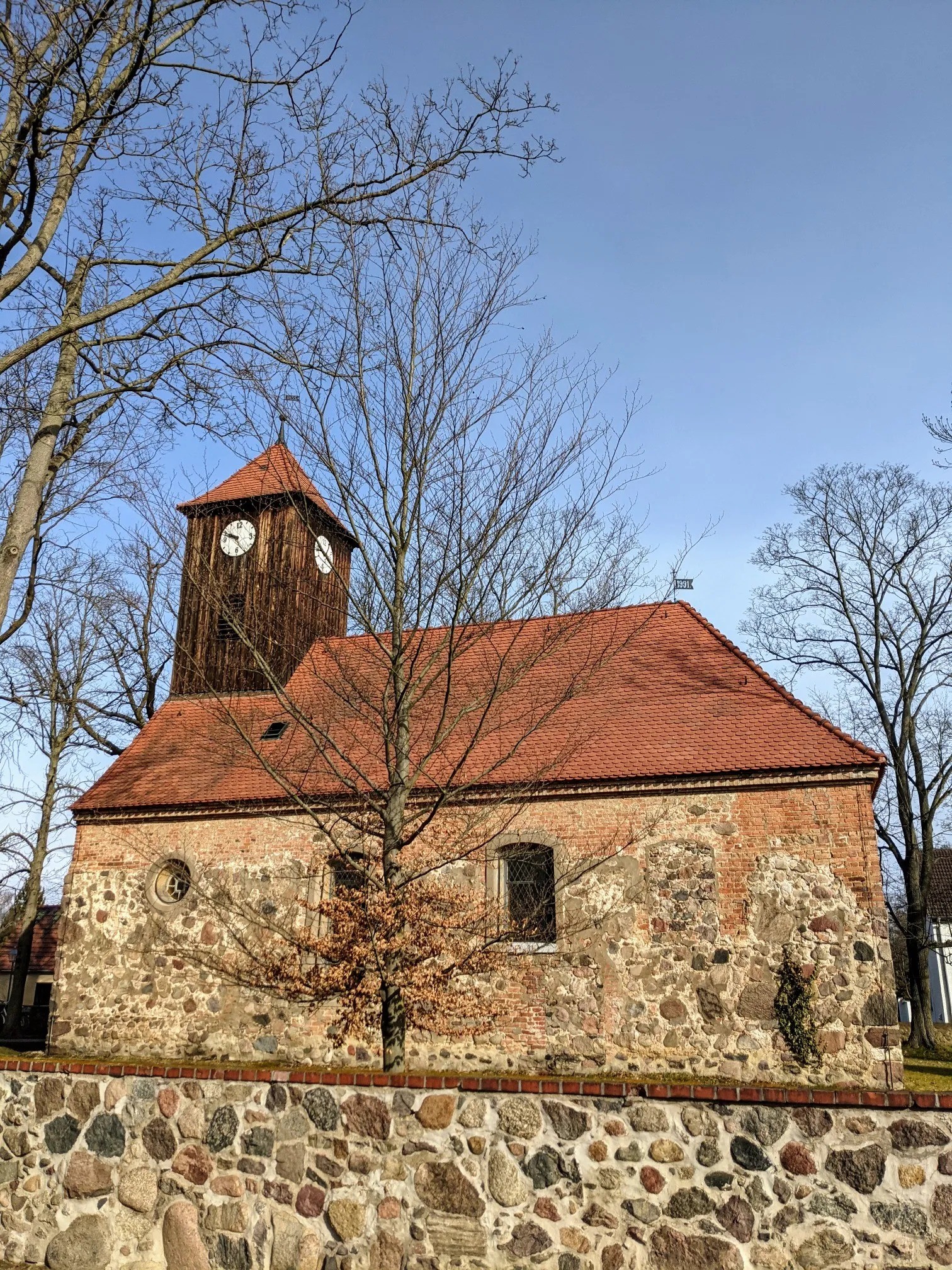 Dorfkirche aus Feldstein und Backstein mit Holzturm und roten Dachziegeln