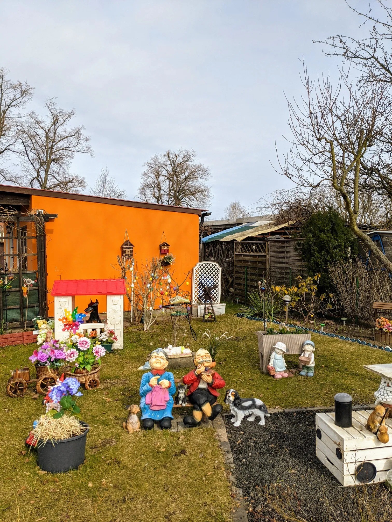 Vorgarten mit bunten Gartenfiguren, Osterbaum und orangefarbener Hauswand