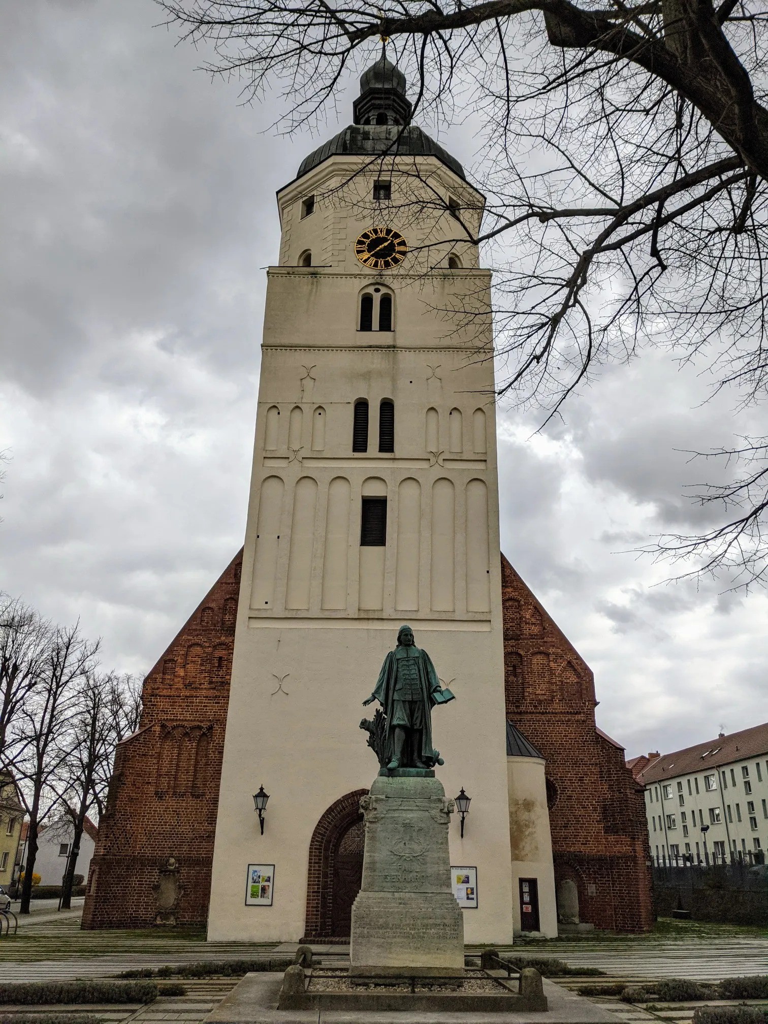 Paul-Gerhardt-Denkmal vor einer weißen Kirche mit Backsteinschiff