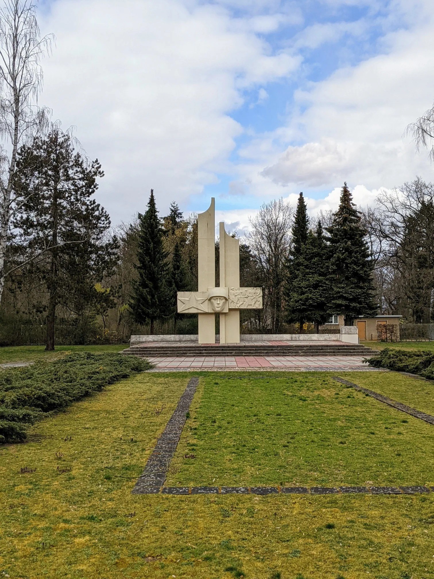Weiße Gedenkanlage in einem Park mit Nadelbäumen