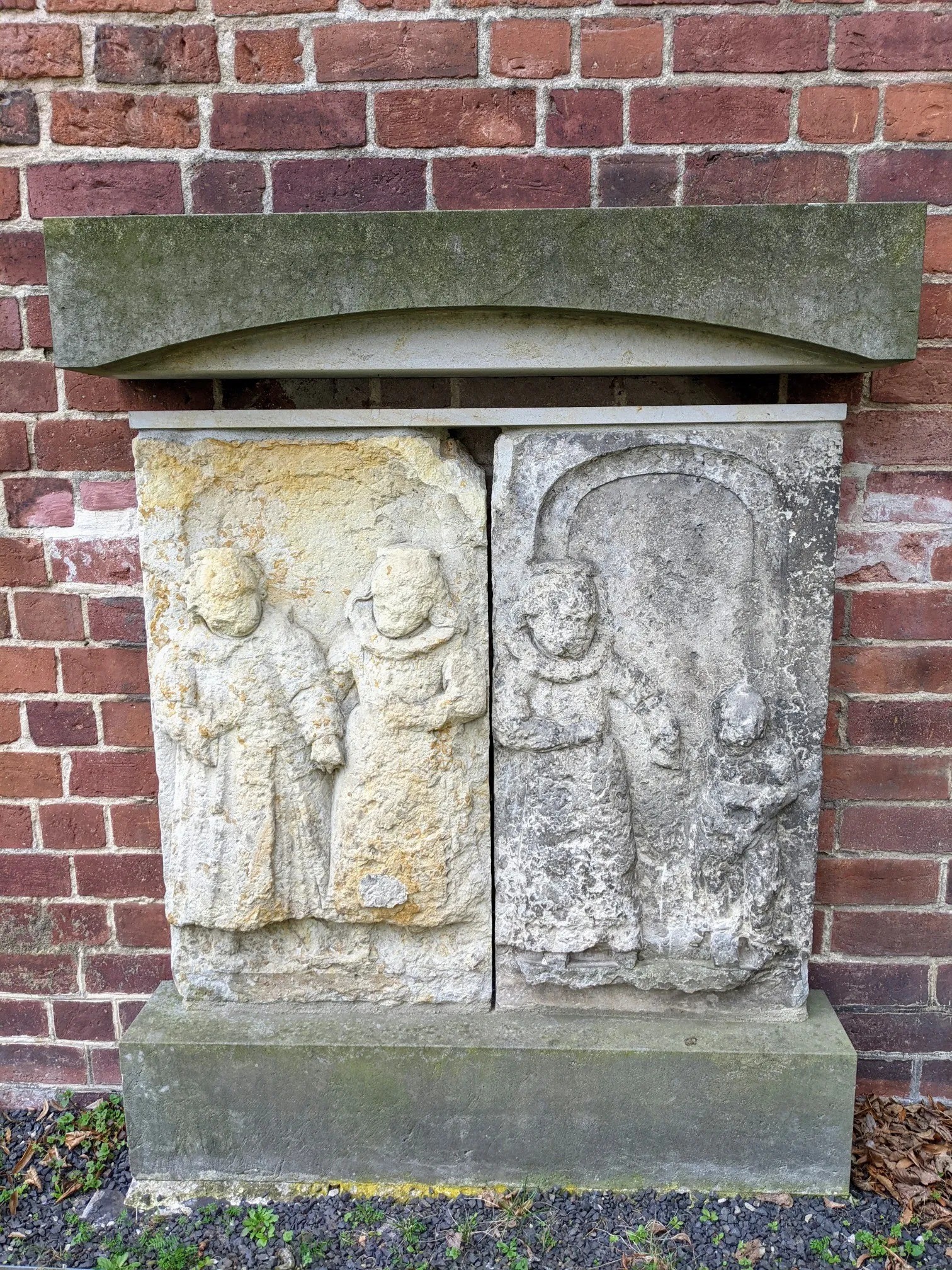 Zwei Sandsteinplatten mit Figuren an einer Backsteinwand