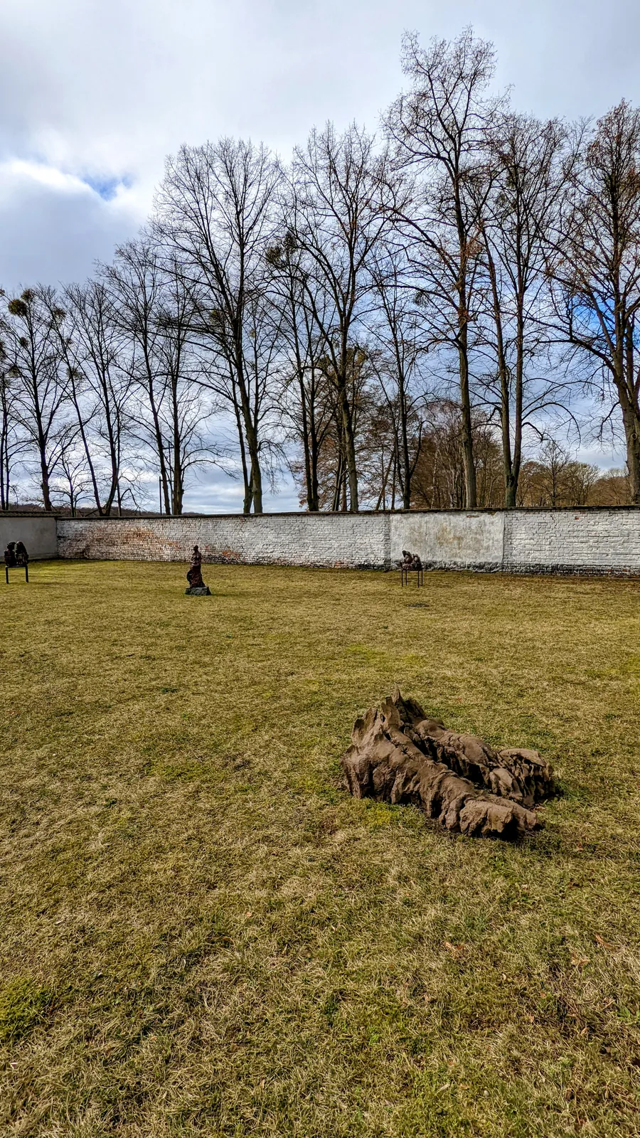 Bronzefigur auf einer Wiese vor der weißen Mauer der Gedenkstätte Ravensbrück