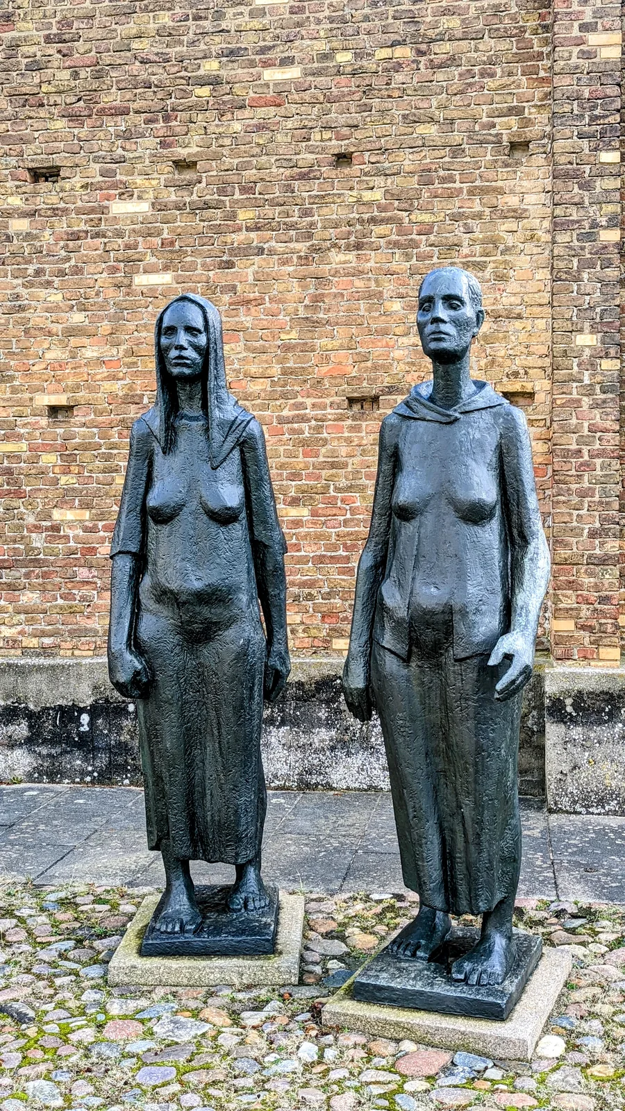 Zwei Bronzefiguren von Frauen vor einer Backsteinwand