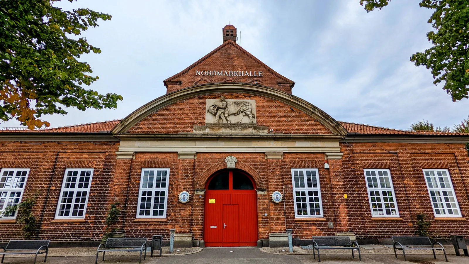 Nordmarkhalle in Rendsburg, Backsteinbau mit roter Tür und Relief über dem Eingang