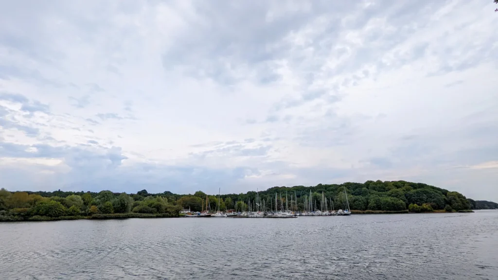 Blick über breites Wasser in Rendsburg, am anderen Ufer Bootsliegeplätze und Bäume
