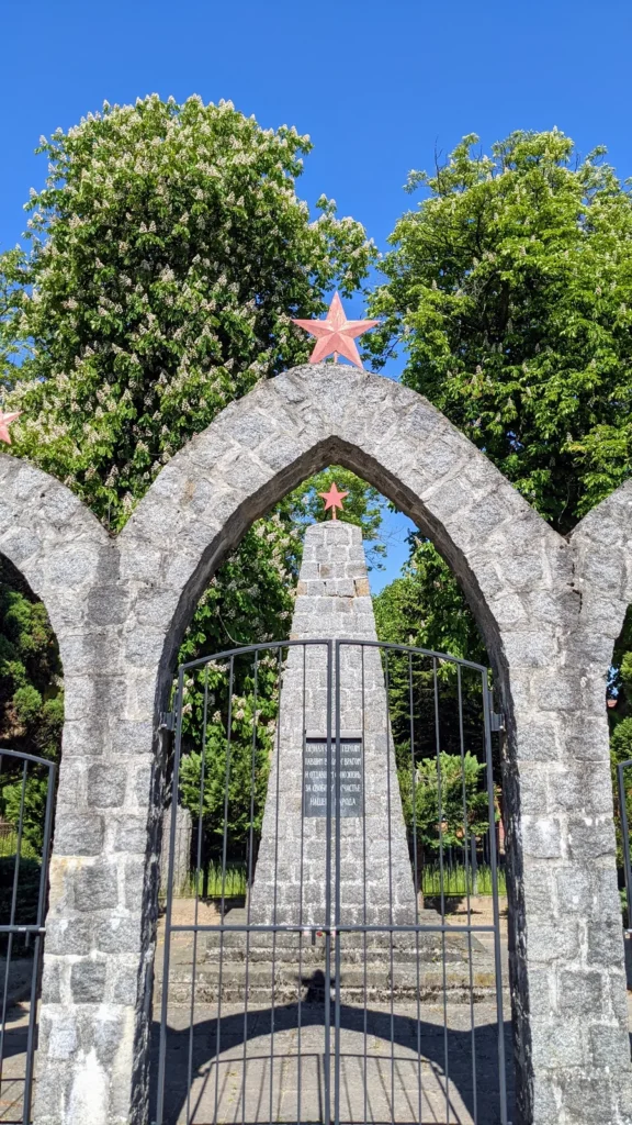 Torbogen aus Feldstein mit rotem Stern am sowjetischen Ehrenfriedhof in Rheinsberg, dahinter ein Obelisk