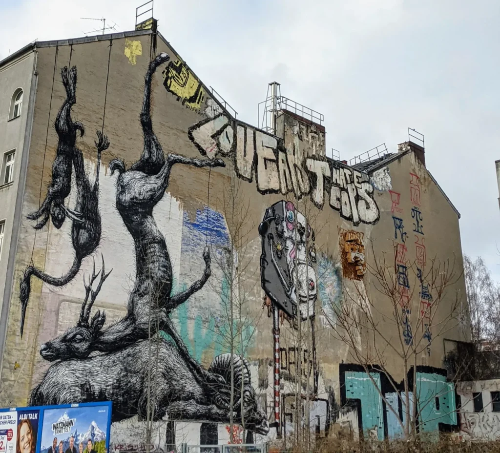 Wandbild Nature Morte von ROA an der Oranienstraße in Berlin-Kreuzberg: tote Tiere in Schwarz-Weiß hängen an Seilen von der Dachkante einer Brandwand