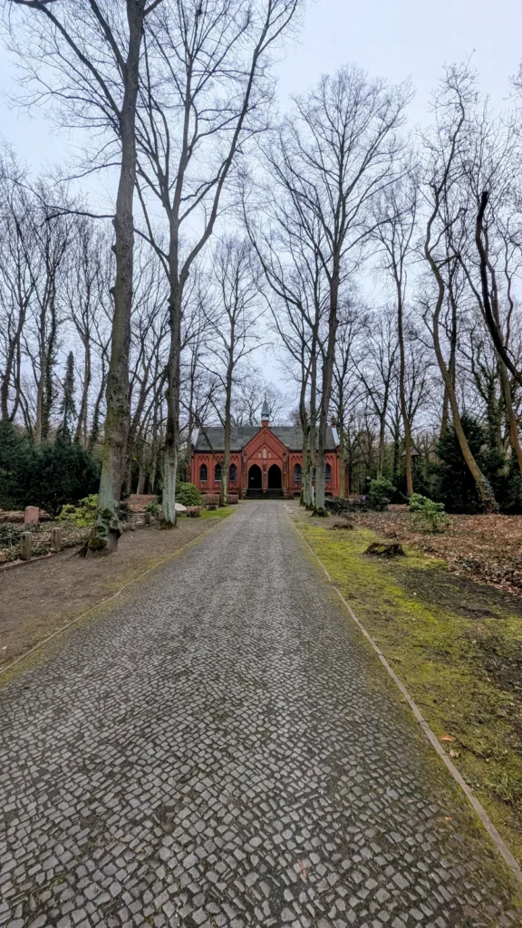 Kopfsteinpflasterweg zwischen kahlen Bäumen auf den Friedhöfen Nordend in Rosenthal, am Ende eine rote Kapelle
