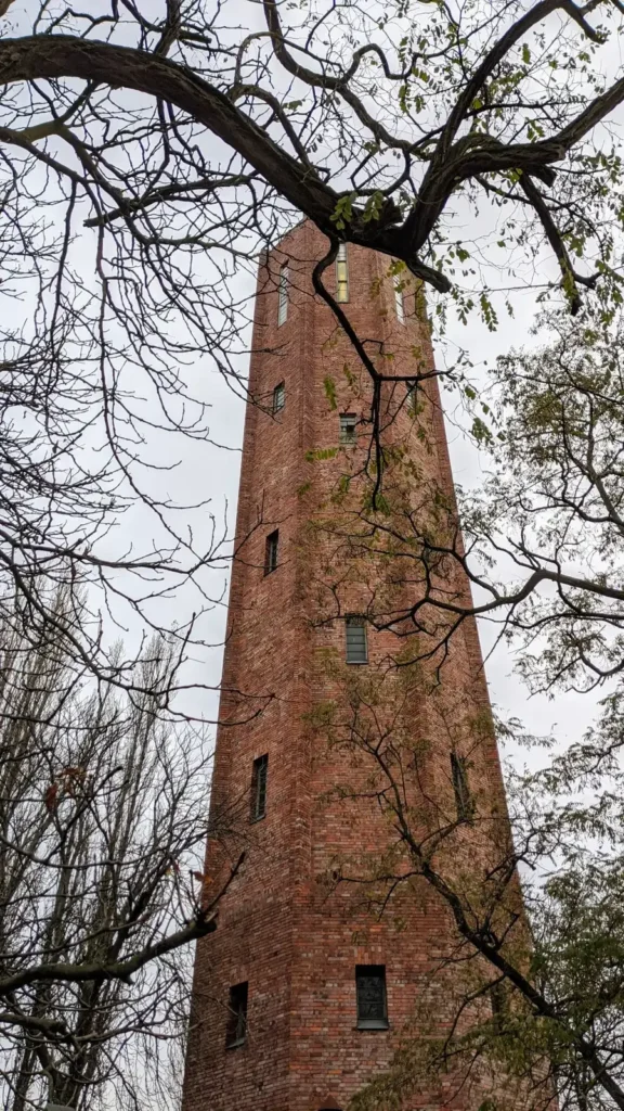Schlanker Backstein-Wasserturm des früheren Gaswerks am Blockdammweg in Rummelsburg, halb verdeckt von Bäumen