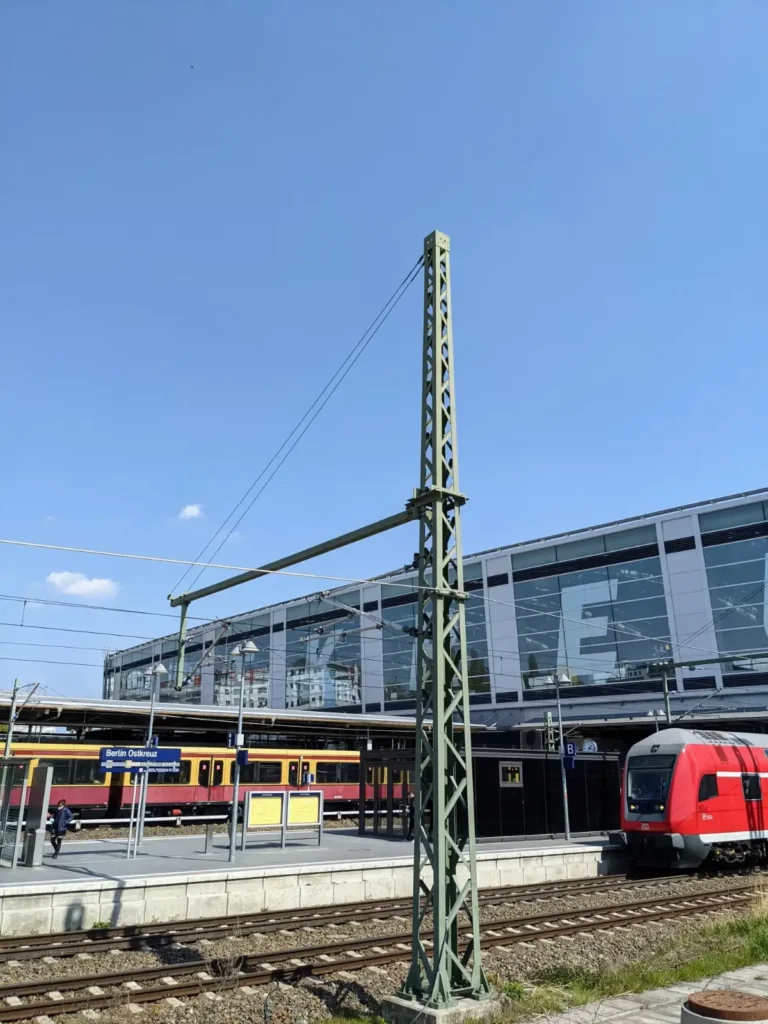 Ringbahnhalle des Bahnhofs Ostkreuz mit großem Schriftzug, davor ein roter Regionalzug