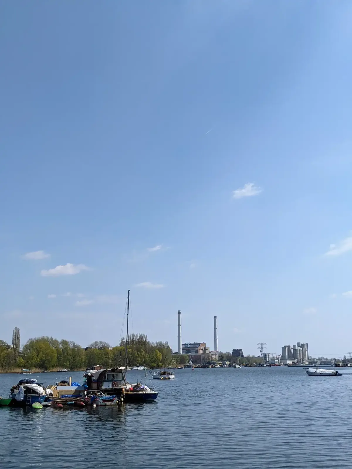 Blick über den Rummelsburger See mit Hausbooten, am anderen Ufer Schornsteine und Neubauten