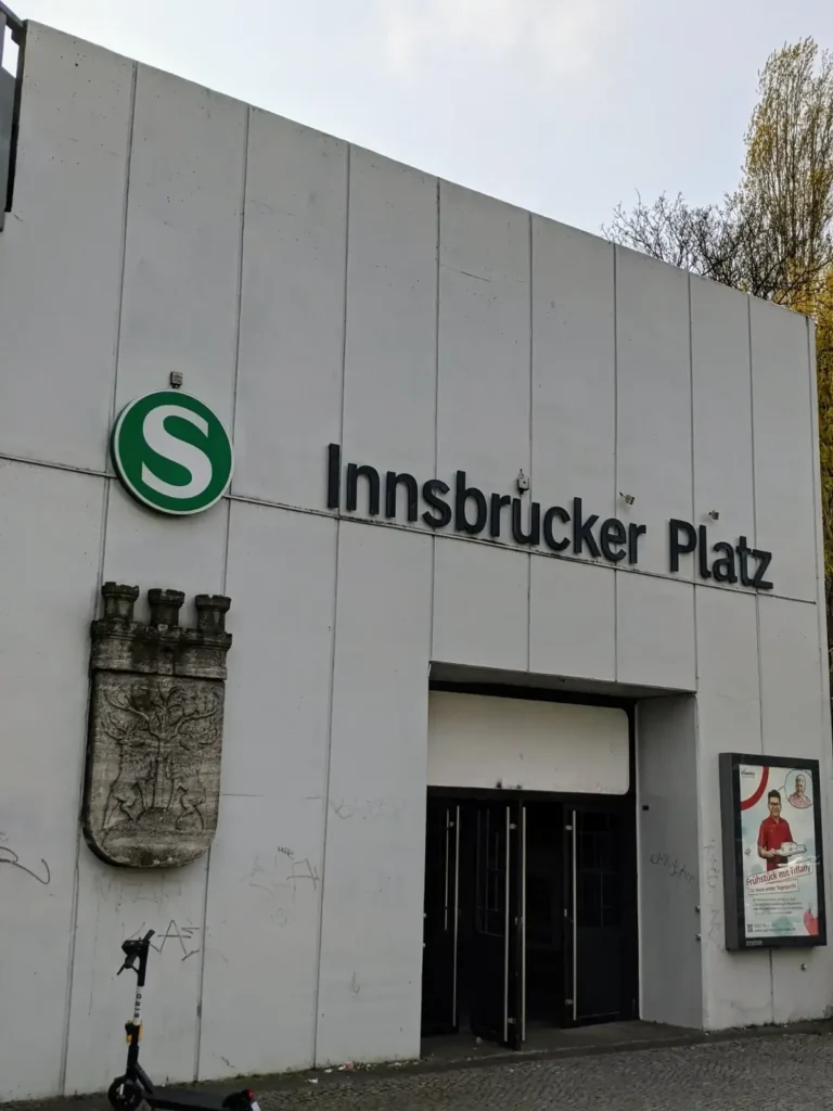 Eingang zum S-Bahnhof Innsbrucker Platz mit Betonplattenwand, S-Zeichen und Wappenrelief