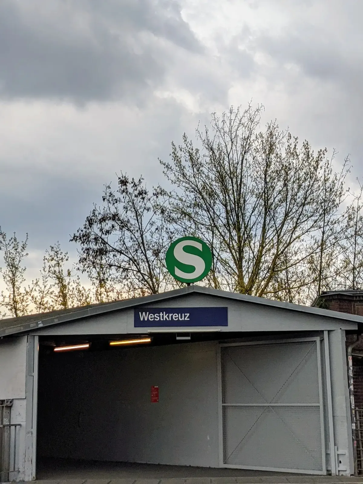 Flacher grauer Zugangsbau des S-Bahnhofs Westkreuz mit Schild und S-Zeichen