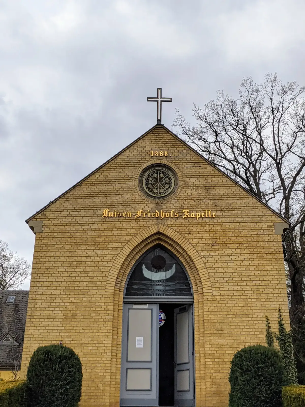 Gelbe Backsteinkapelle des Luisenfriedhofs II in Berlin-Westend mit Kreuz, Rosette und goldener Inschrift