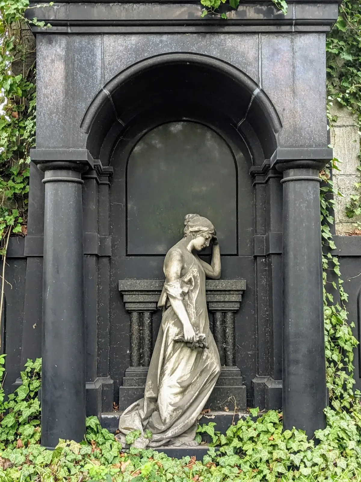 Schwarzes Wandgrab mit Säulen und weißer Marmorfigur einer Trauernden auf dem Luisenfriedhof II in Berlin