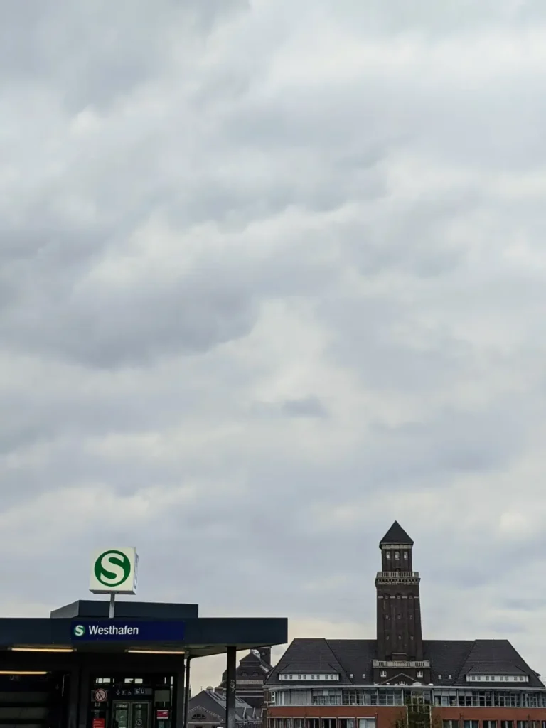 Bahnsteigdach mit Schild am Bahnhof Westhafen in Berlin, dahinter der Turm des Westhafen-Verwaltungsgebäudes