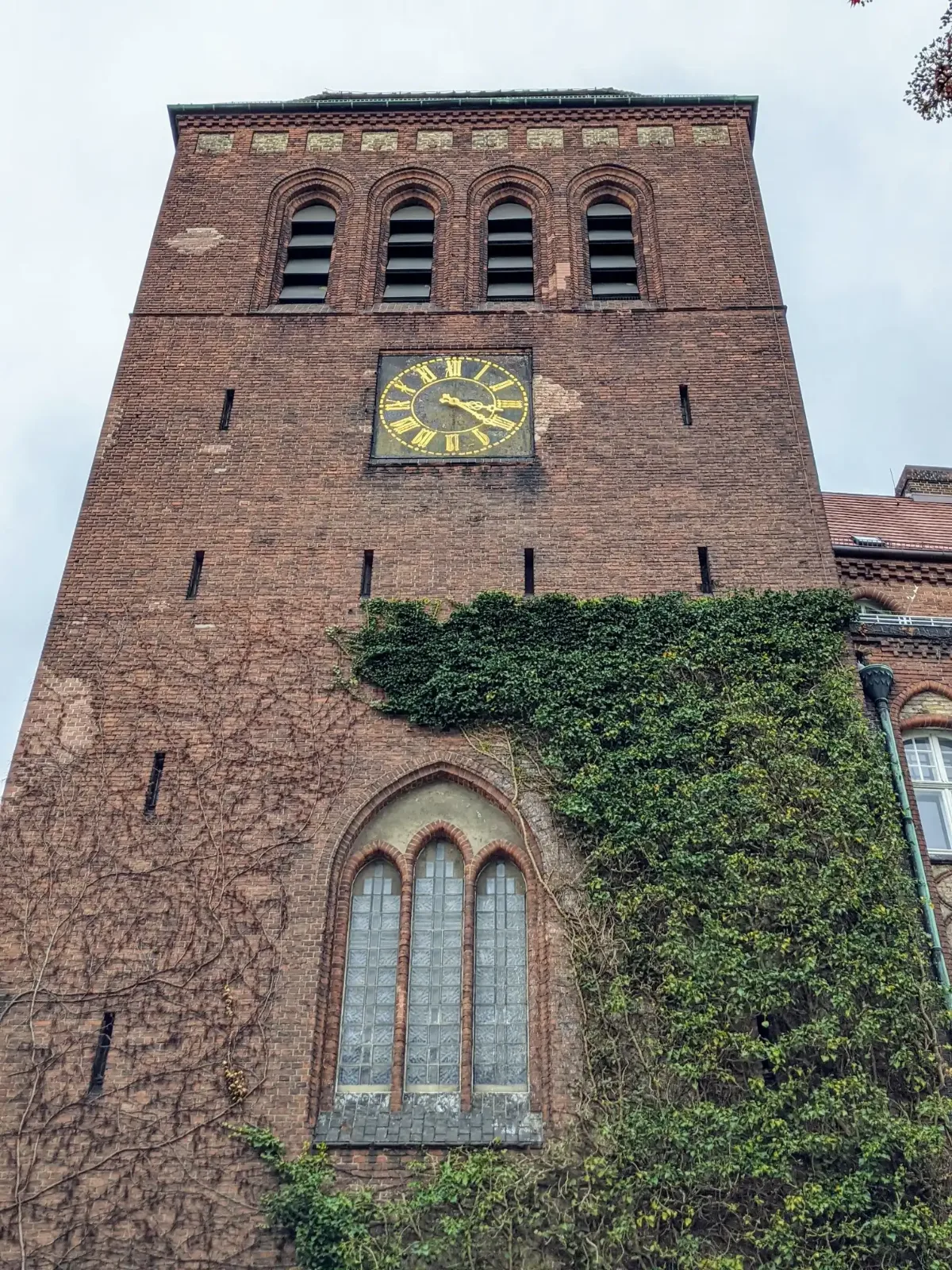 Backsteinturm der Osterkirche an der Samoastraße in Berlin-Wedding mit goldener Uhr und Efeu