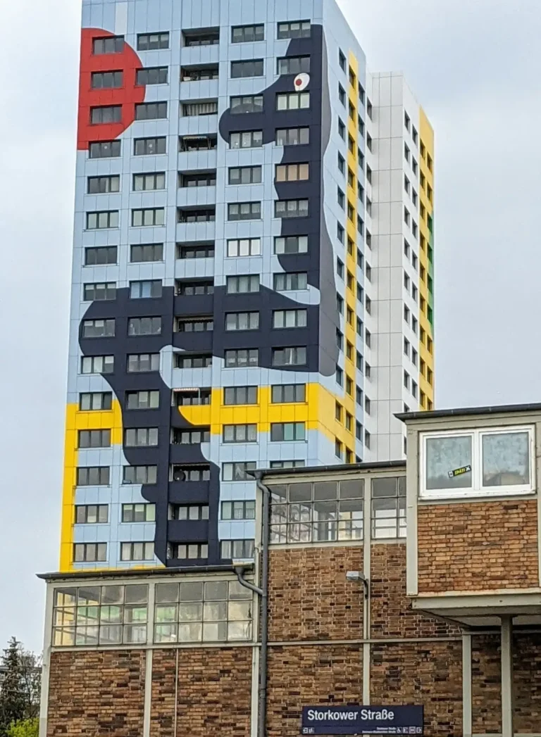 Backstein-Zugang des S-Bahnhofs Storkower Straße, dahinter das bunte Gustavo-Haus