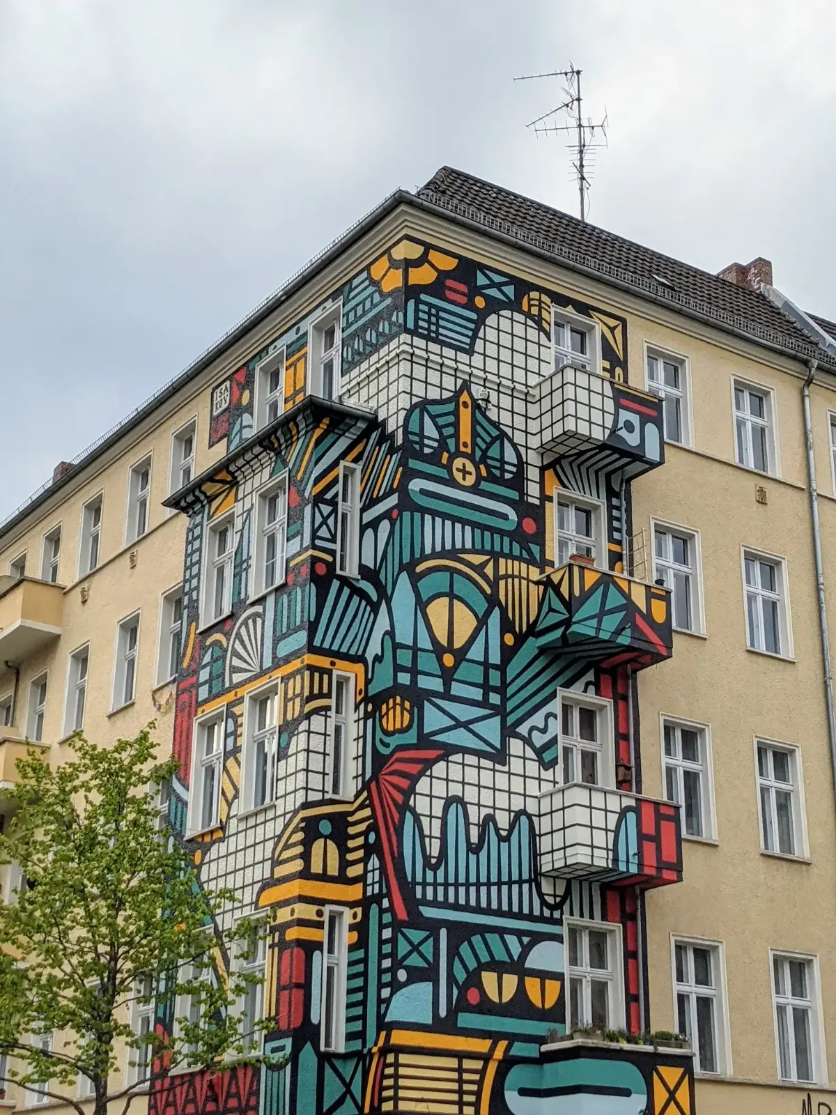 Grafisches Wandbild in Türkis, Gelb, Rot und Schwarz an einem Altbau-Eckhaus im Friedrichshainer Nordkiez