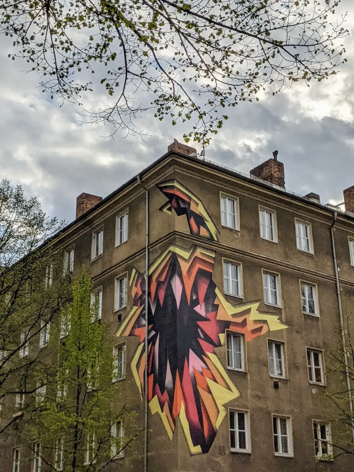 Wandbild mit abstraktem Vogel in Rot, Orange, Gelb und Schwarz an einer Altbau-Ecke in Friedrichshain