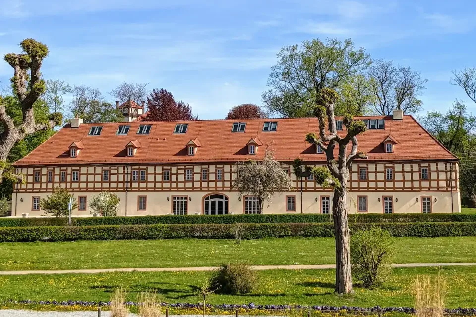 Langgestrecktes Gebäude mit rotem Dach hinter einem Wasserlauf im Schlosspark Lübbenau
