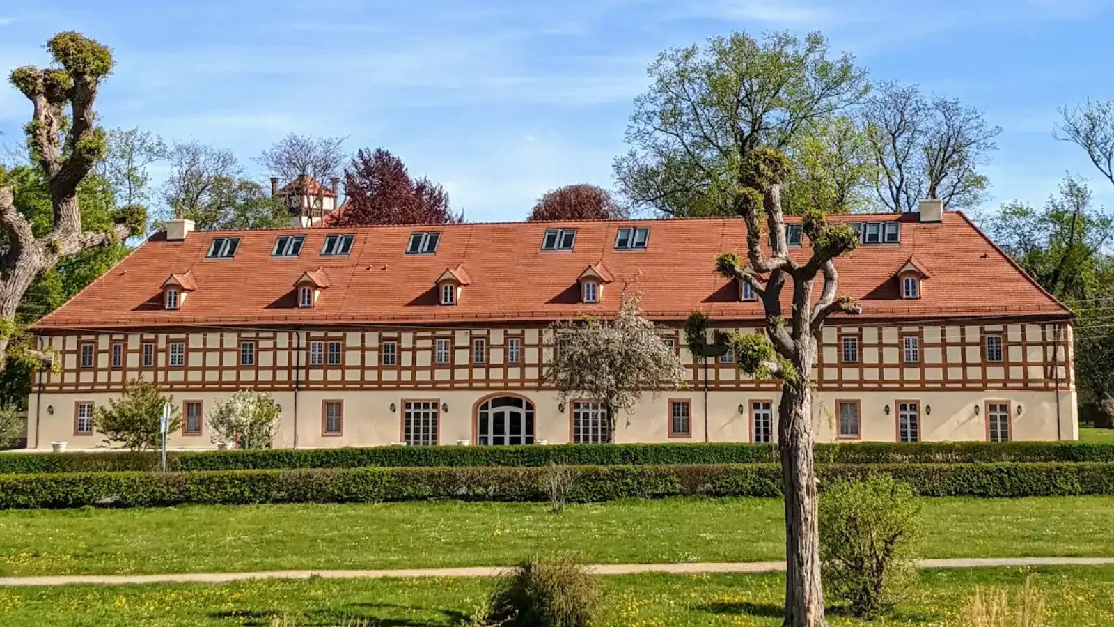Langgestrecktes Gebäude mit rotem Dach hinter einem Wasserlauf im Schlosspark Lübbenau