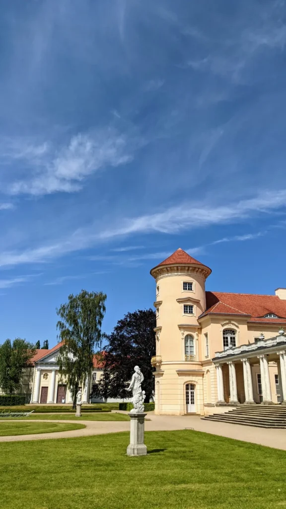 Kolonnade und Turm von Schloss Rheinsberg mit einer Statue im Garten