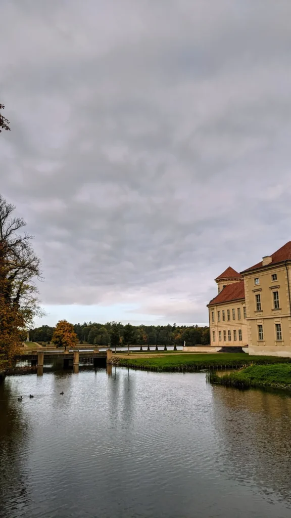 Wasserlauf im Park mit Steg, dahinter ein Flügel von Schloss Rheinsberg