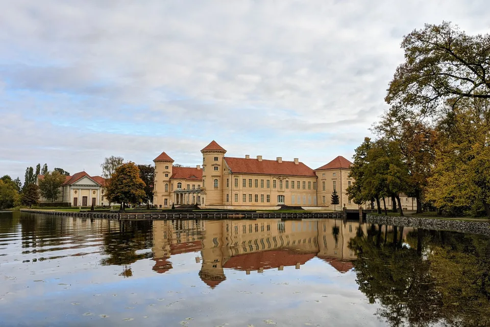 Schloss Rheinsberg am Ufer des Grienericksees, davor Herbstbäume und die Spiegelung im Wasser