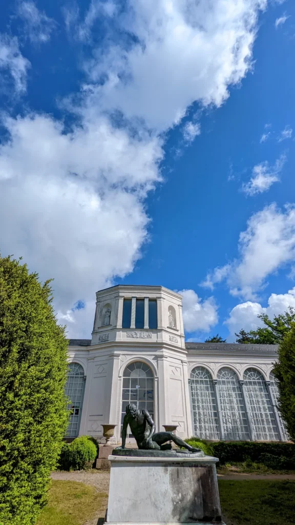 Seitenflügel der Orangerie Putbus mit hohen Rundbogenfenstern, davor eine liegende Bronzefigur