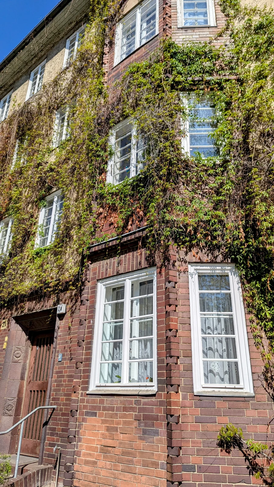 Rotes Backsteinhaus mit weißen Sprossenfenstern, Fassade teilweise von Efeu bewachsen, im Ortskern von Schmargendorf