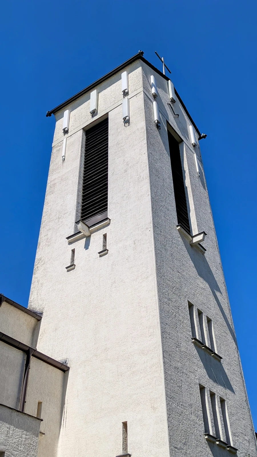 Weiß verputzter Kirchturm mit Kreuz und dunklen Schallöffnungen vor blauem Himmel in Schmargendorf