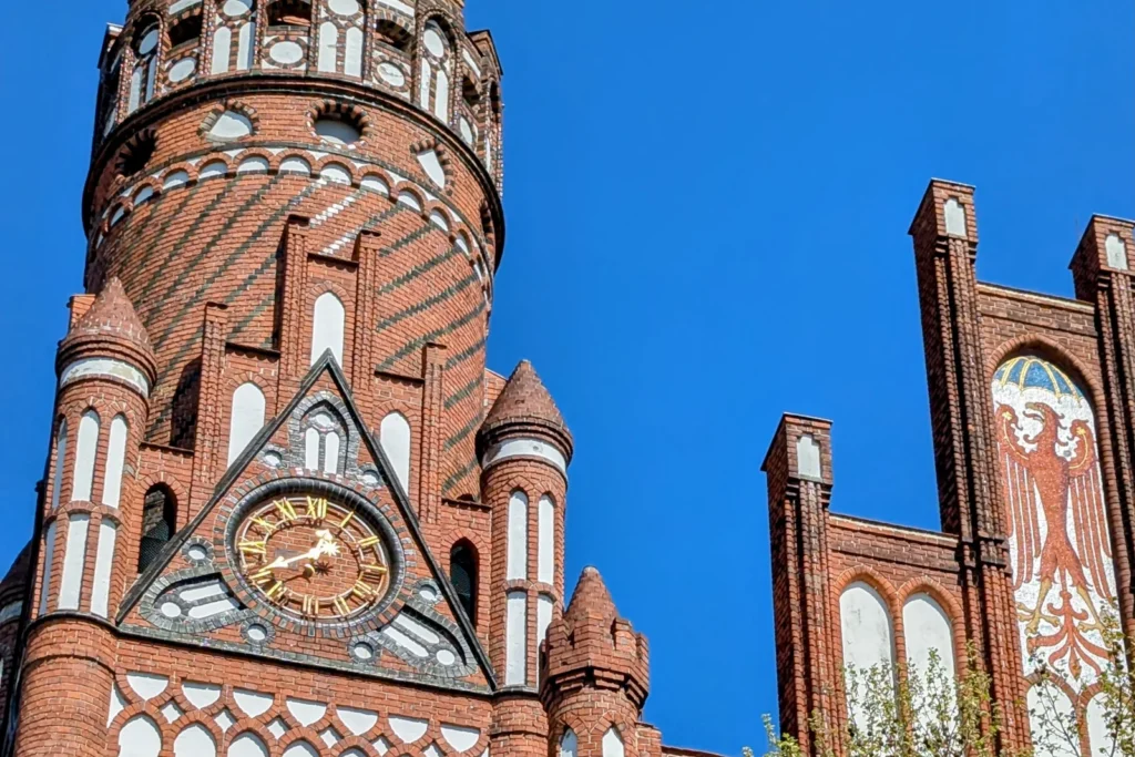 Backsteinturm des Rathauses Schmargendorf mit Uhr, Zinnenkranz und Giebeln vor blauem Himmel
