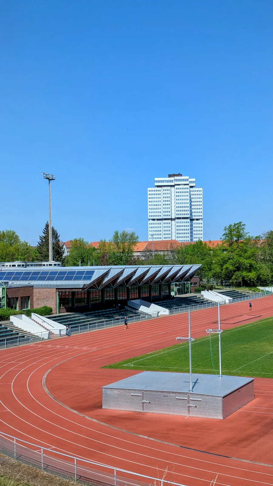 Leichtathletikanlage mit roter Laufbahn und Tribüne im Stadion Wilmersdorf, dahinter ein Hochhaus