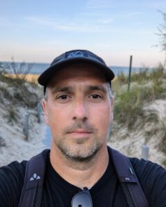 Sebastian mit Schirmmütze und Rucksack auf einem Dünenweg, im Hintergrund das Meer