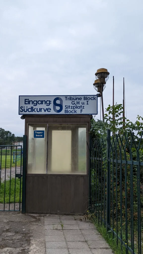 Kassenhäuschen am Eingang Südkurve des Stadions am Quenz mit blauem Wegweiser zu Tribüne und Stehplatz