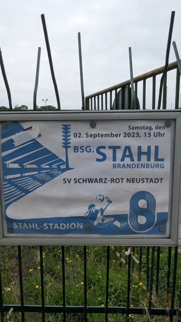 Blau-weißes Spielplakat am Stadionzaun: BSG Stahl Brandenburg gegen SV Schwarz-Rot Neustadt im Stahl-Stadion