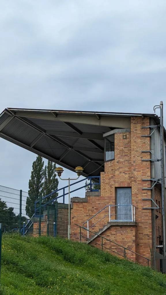 Seitenansicht der überdachten Tribüne im Stadion am Quenz mit Backsteinsockel und weit auskragendem Dach