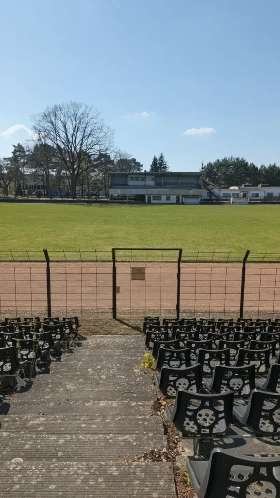 Blick von den Sitzreihen über die Aschenbahn und den Rasen auf die Tribünenseite des Stadions der Hüttenwerker