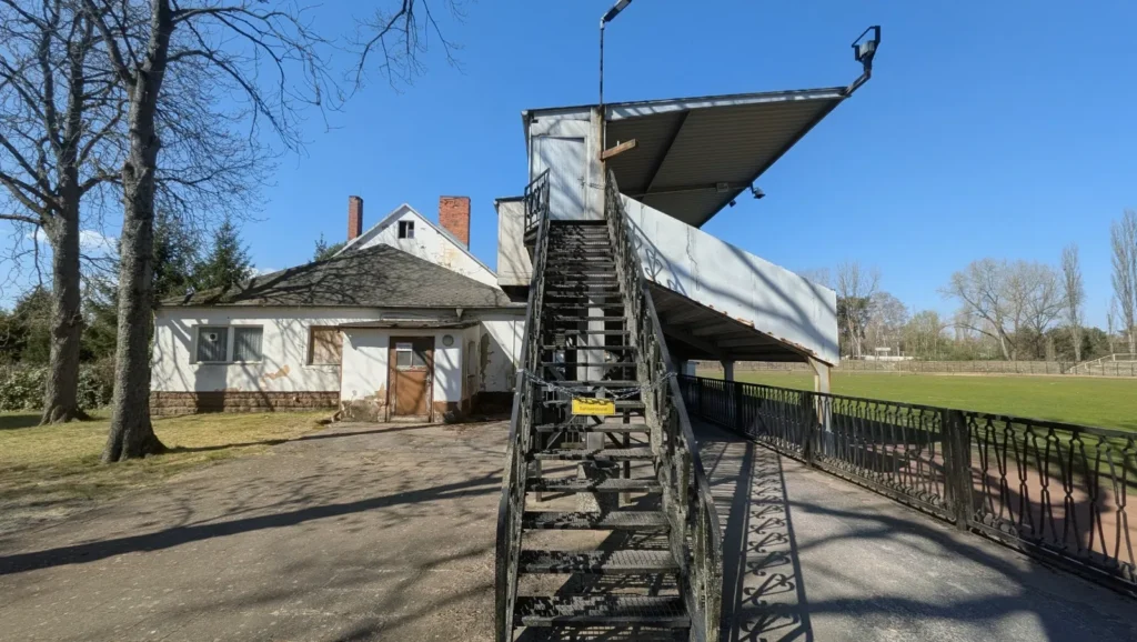 Haupttribüne des Stadions der Hüttenwerker von hinten mit Treppe, links ein weißes Funktionsgebäude