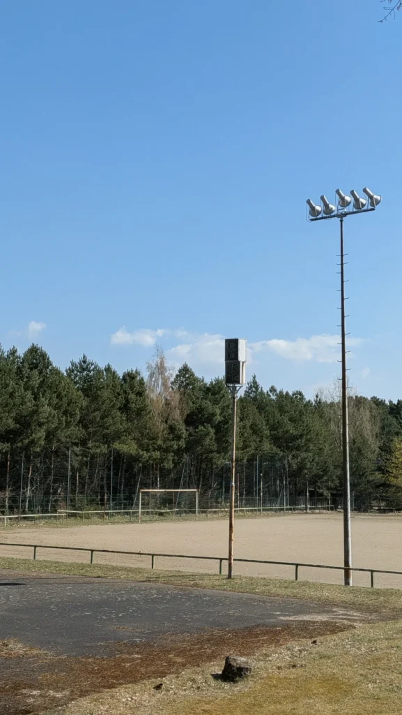 Hartplatz neben dem Stadion der Hüttenwerker mit Flutlichtmast, Tor und Kiefernwald
