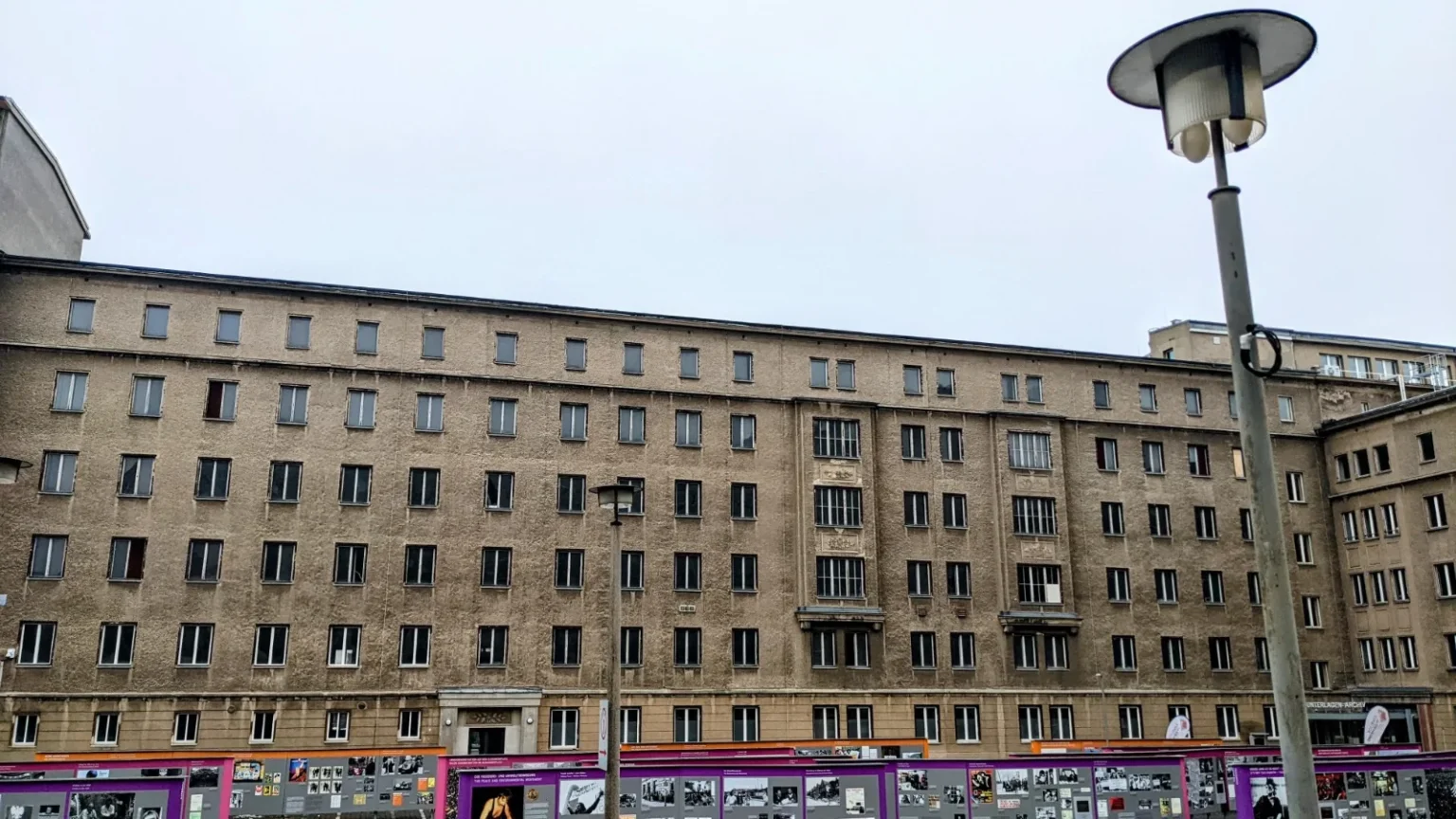 Lange Gebäudefront der ehemaligen Stasi-Zentrale in Berlin-Lichtenberg, im Erdgeschoss Tafeln einer Freiluftausstellung
